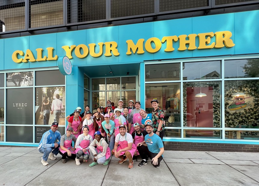 a group of people wearing pink aprons posing in front of a teal storefront