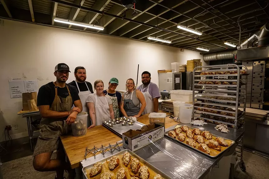 A group of bakers posing in front of baked goods in a kitchen