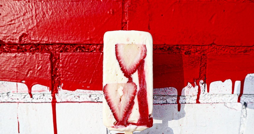 a popsicle with strawberry slices in it in front of a red and white wall