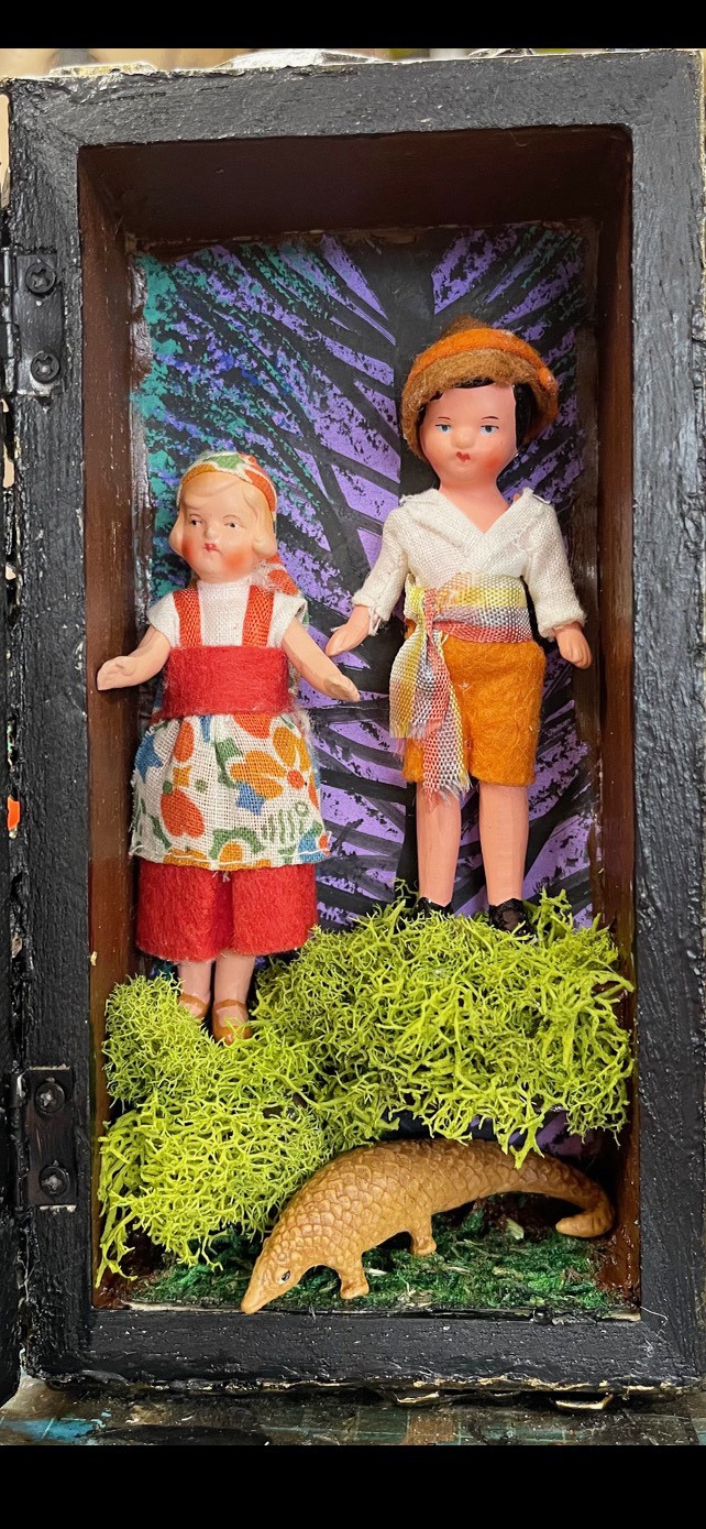 two plastic baby dolls in a diorama with a dinosaur