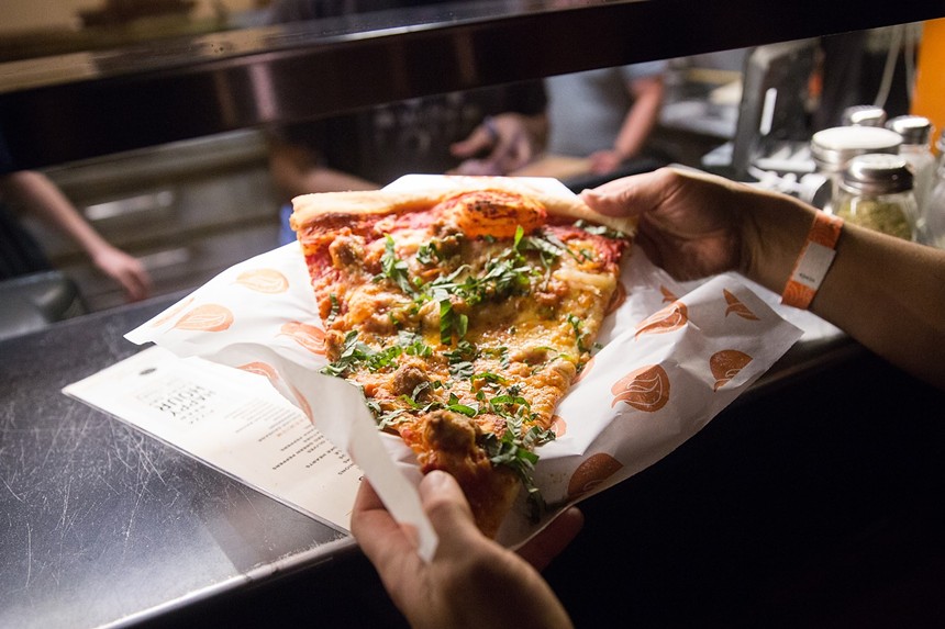 hands holding a slide of pizza on parchment paper