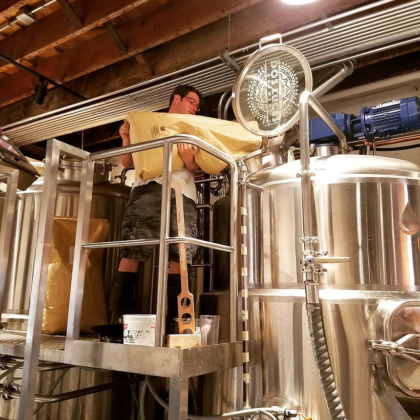 a man holding a bag and pouring hops into brewing equipment