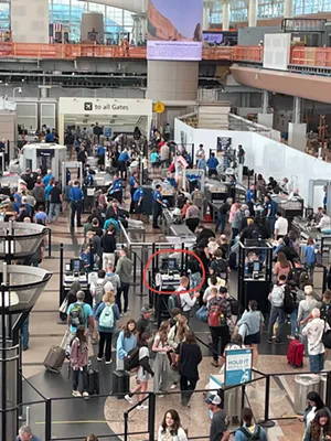 Amidst people moving through a security checkpoint, a screen is circled in red.