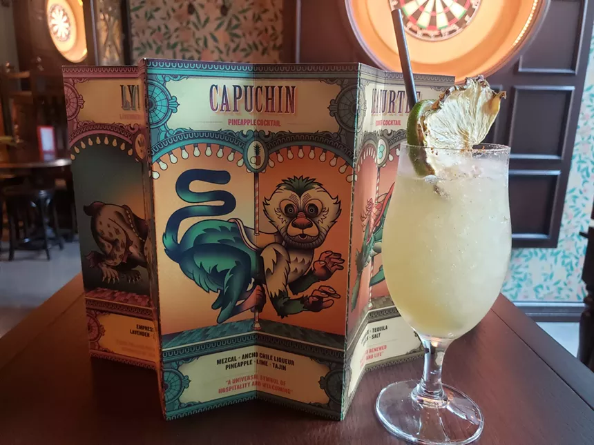 a menu stading upright on a table with a yellow-colored cocktail in front of it