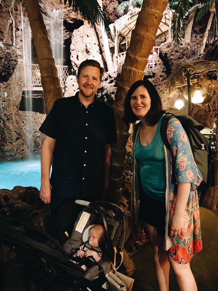 a man and a woman with a baby in a stroller in front of an indoor pool with a waterfall