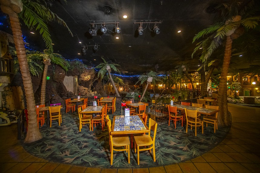 a dining room with tables, chairs and fake palm trees