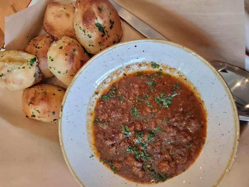 a bowl of red chili next to several garlic knots