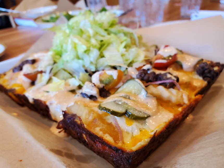 a rectangular pizza topped with pickles, ground beef, thousand island dressing and a pile of shredded lettuce