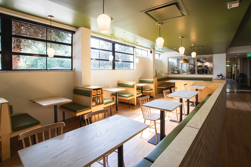 the inside of an empty restaurant with wooden tables and green accents