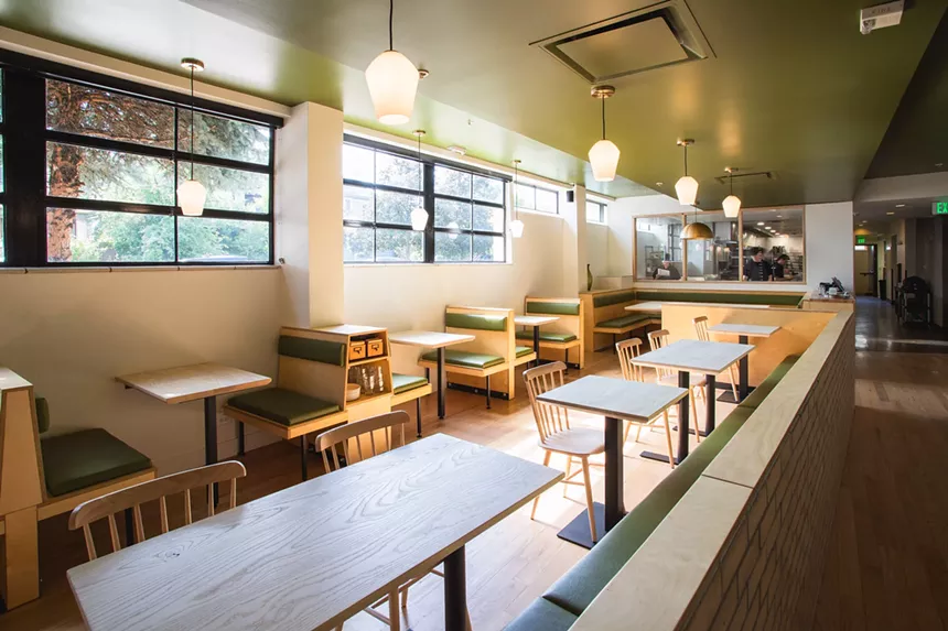 the inside of an empty restaurant with wooden tables and green accents