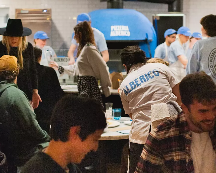people inside of a restaurant with a blue pizza oven in the background
