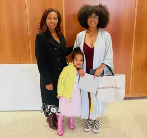 two women and a child standing in front of a wooden wall