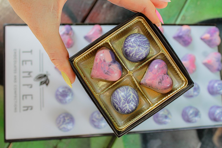 a hand holding a box with four colorful chocolates inside