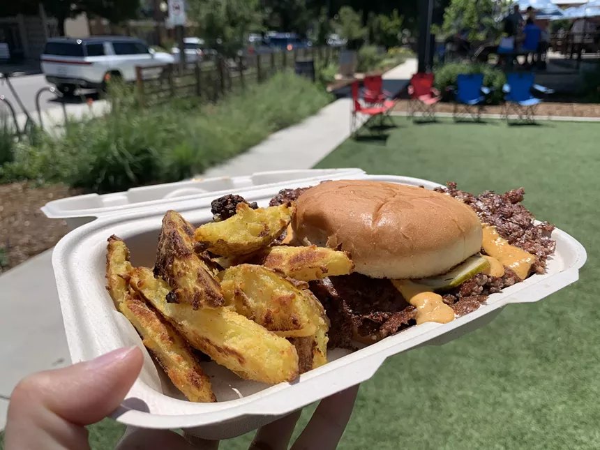hand holding a to go box with potato wedges and a burger inside