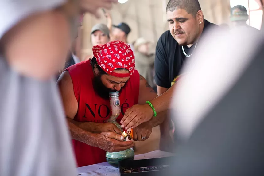 A man smokes weed from a bong with friends