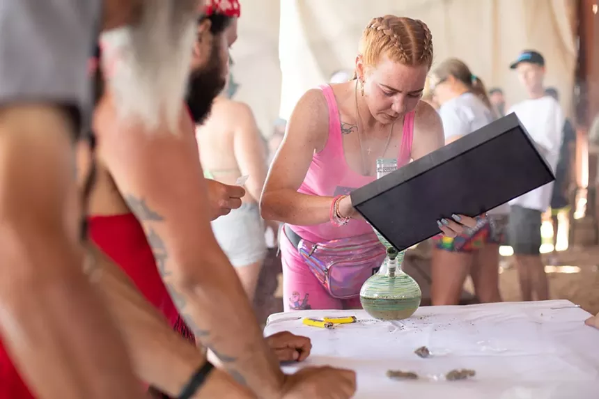 A woman in pink loads cannabis into a bong at a party