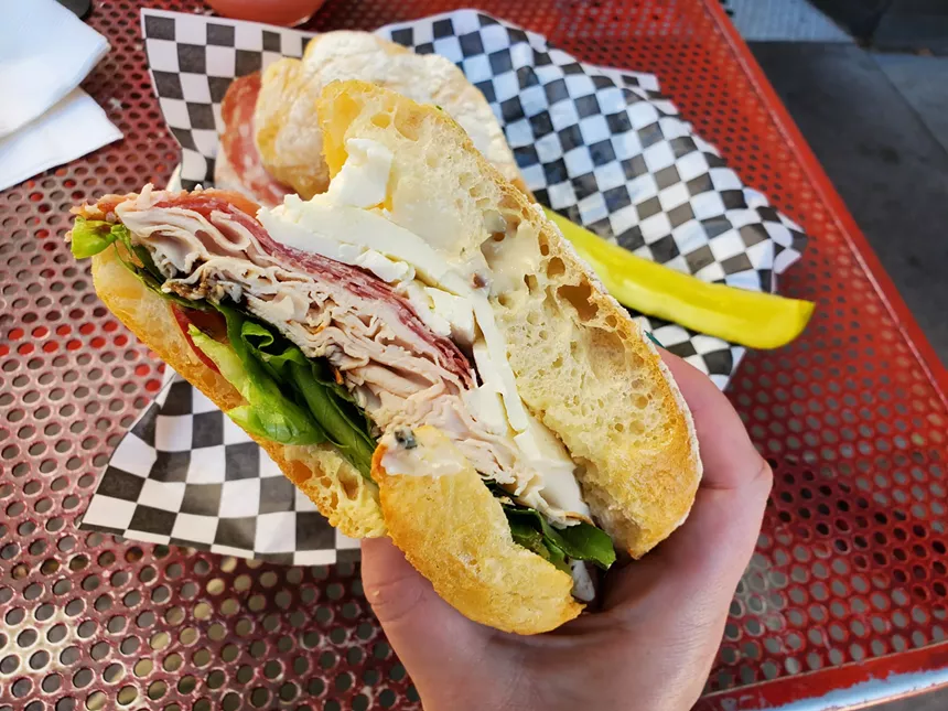hand holding a sandwich with deli meat and cheese