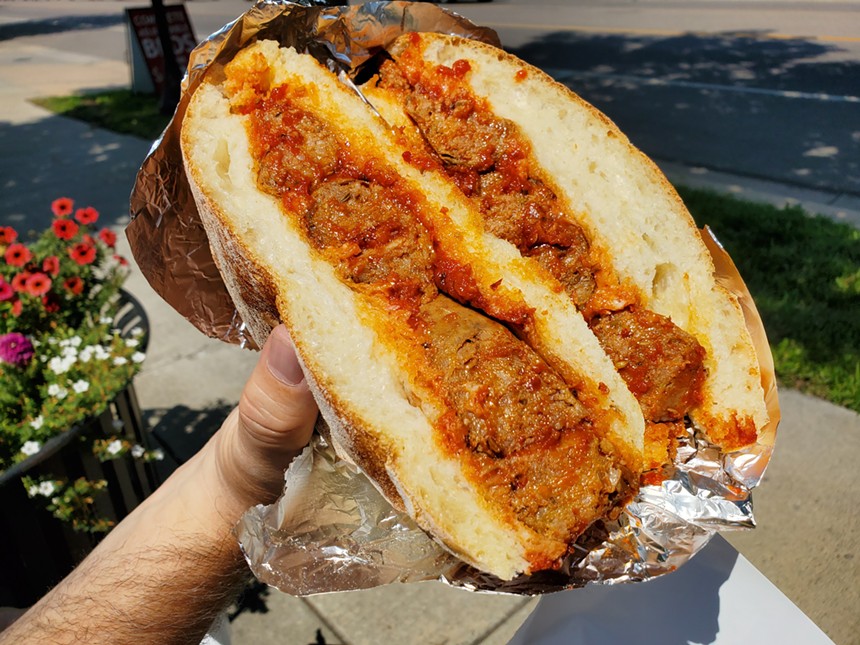 hand holding a sandwich with Italian sausage and red sauce