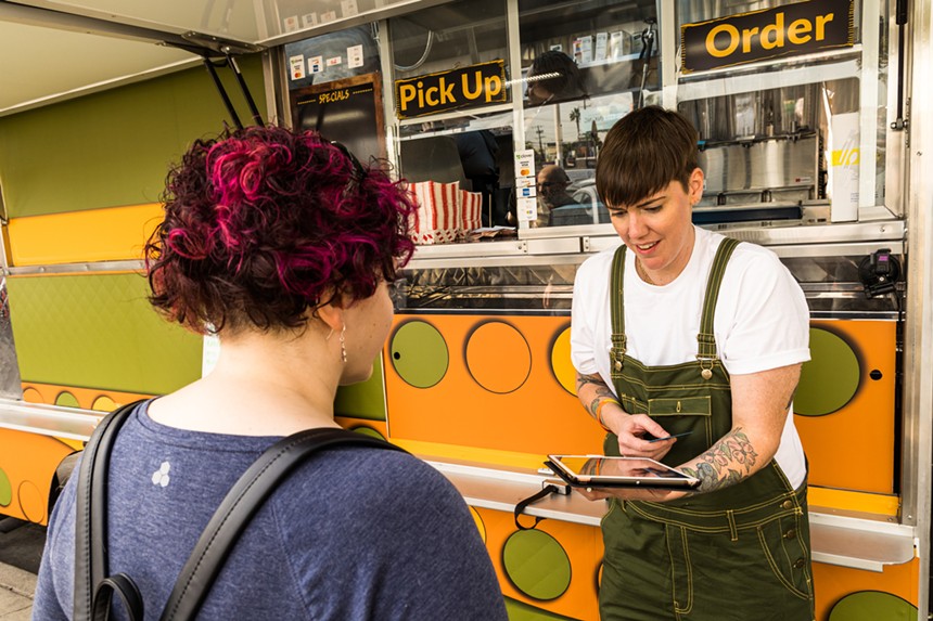 person in an apron standing in front of a food truck taking an order from another person