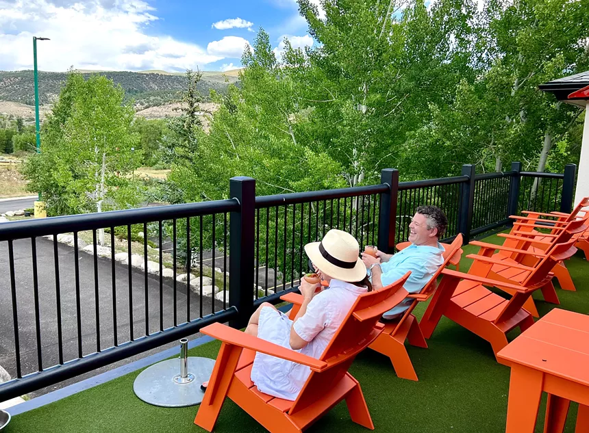two people sitting in orange patio chairs facing trees and hills