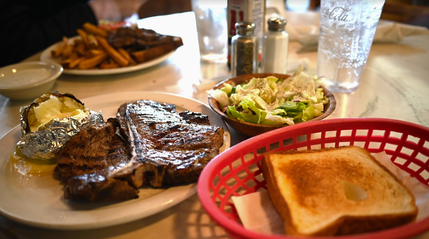 a piece of break in a basket bnext to a t bone steak on a plate and a salad