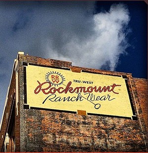 A yellow sign saying Rockmount Ranchwear on a brick building against the sky.