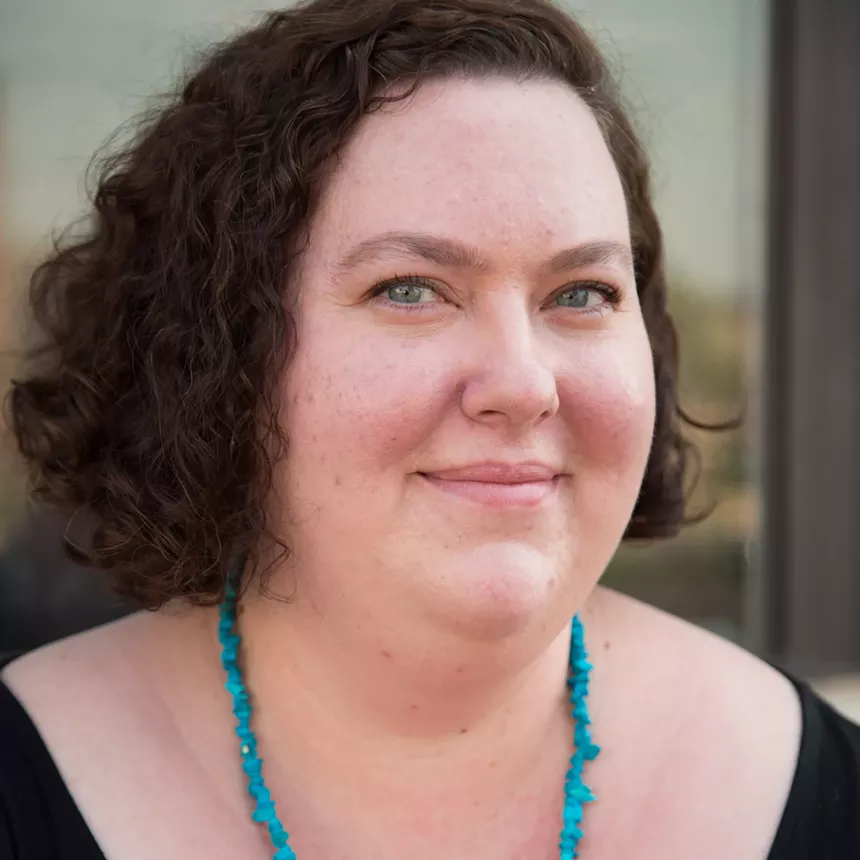 a woman with dark brown hair and blue eyes wearing a turquoise necklace and black shirt.