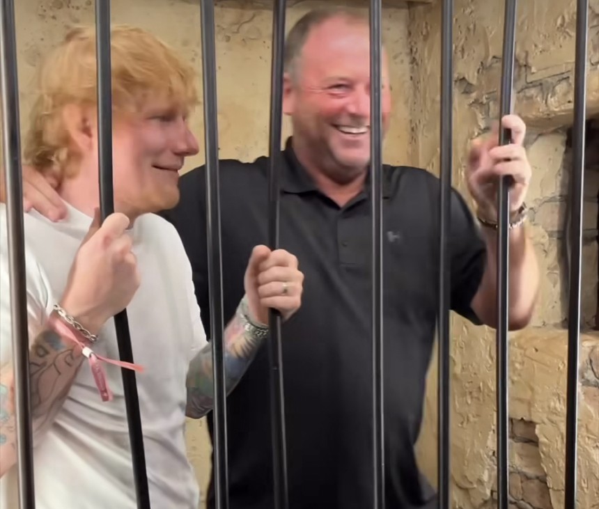 a ginger man in white t shirt next to bald man in black shirt, both standing behind bars.
