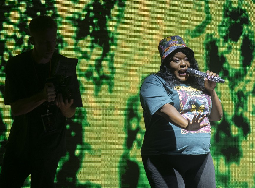 woman wearing a bucket hat sings into a crystal-covered microphone