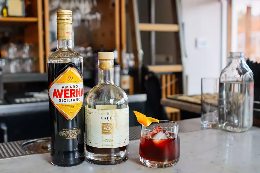 liquor bottles sit on bar with red cocktail in glass