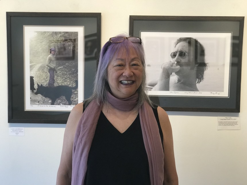 woman with purple hair and scarf posing in front of photos of John Lennon