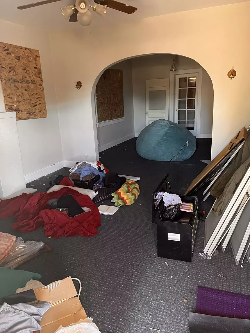 A living room with piles of clothes and other trash on the floor.