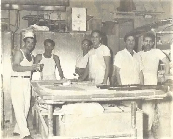 a black and white photo of men in the back of a bakery