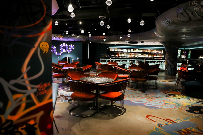 a lounge with tables, chairs and graffiti on the floor and ceilings