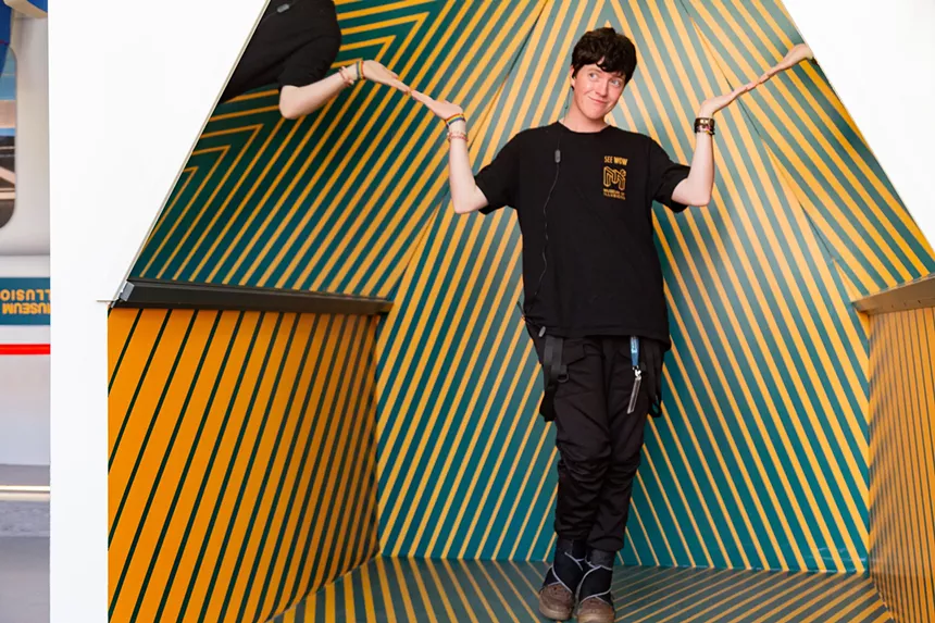 person with short brown hair stands in a striped room with mirrors on the ceiling.