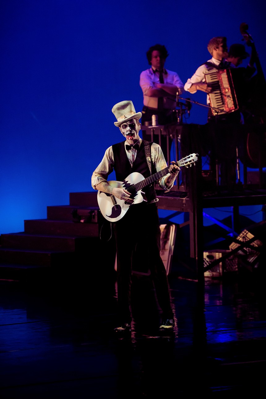 man with skeleton makeup and top hat playing guitar