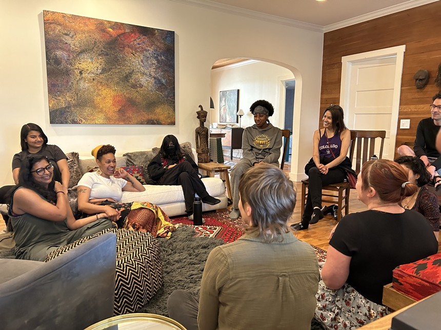 A group of women sits in a circle, some on couches and some on the floor.