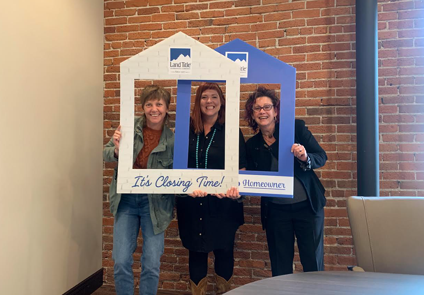 Three women smile while putting their faces through pentagon-shaped frames.