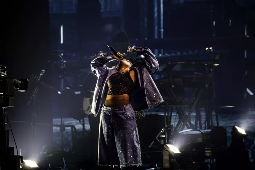 woman throwing her head back while singing into a mic on stage