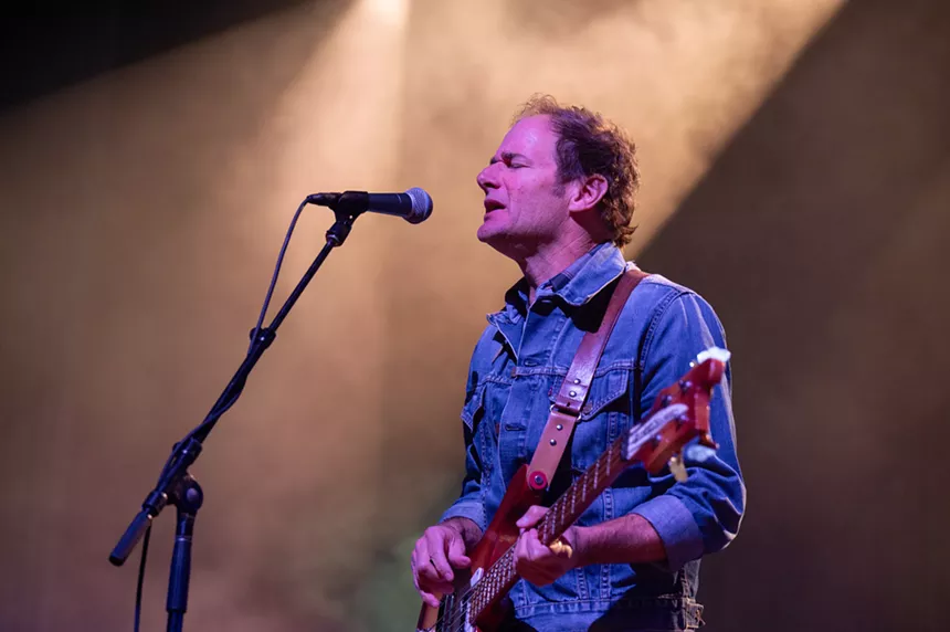 man in jean shirt playing bass and singing into a microphone