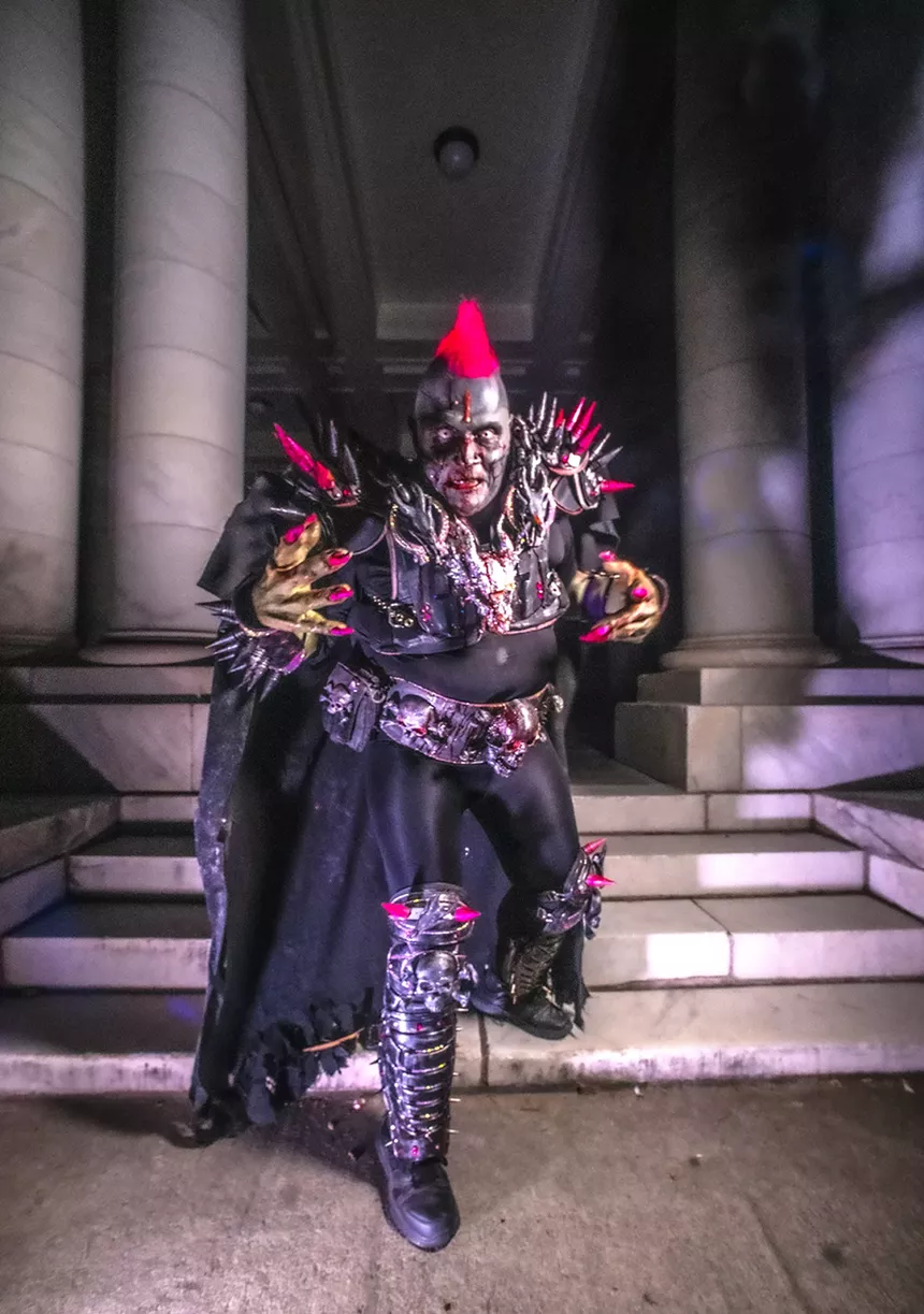 man in zombie facepaint with fake blood has a pink mohawk and is wearing spiky armor