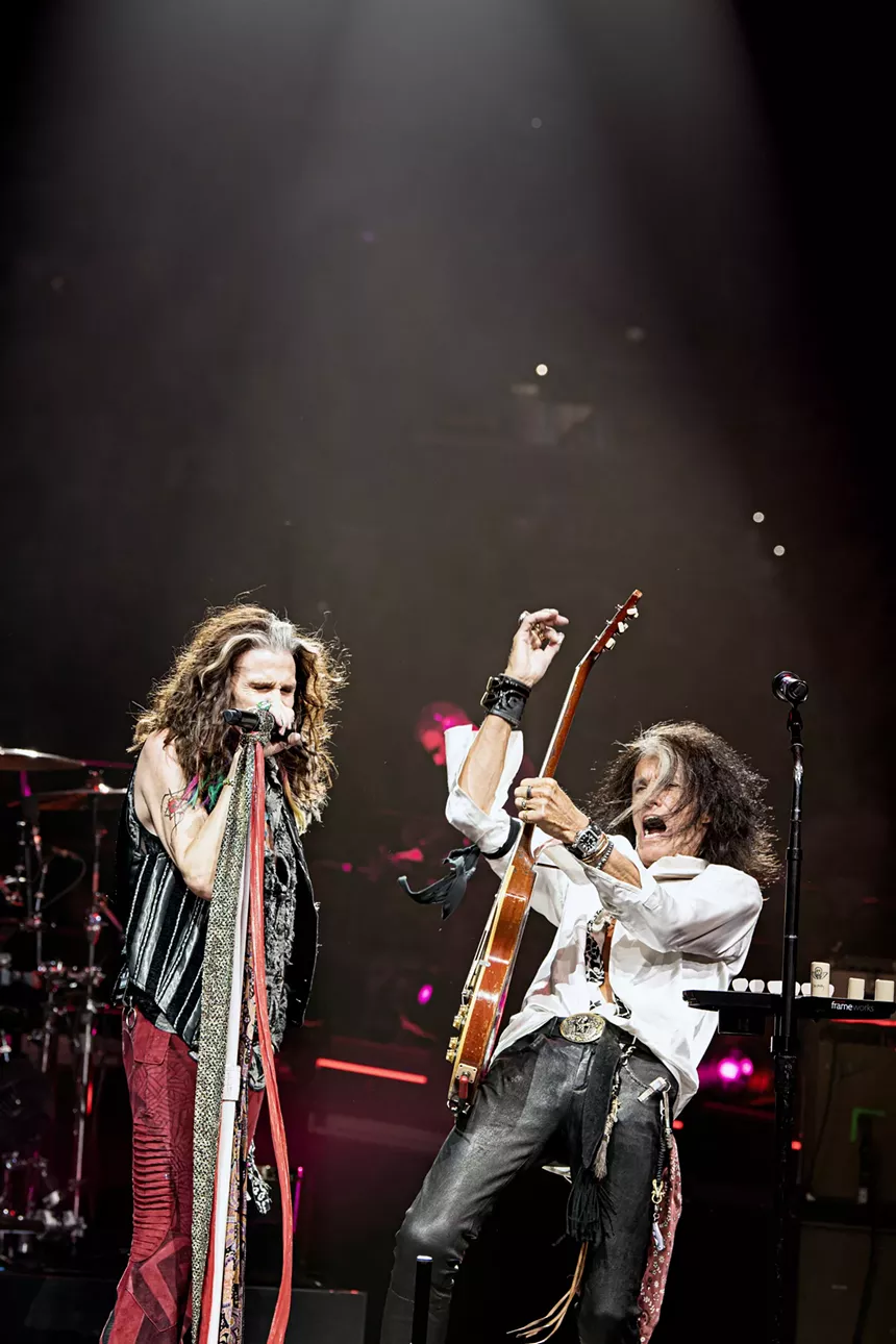 man sings into a microphone while another plays the guitar