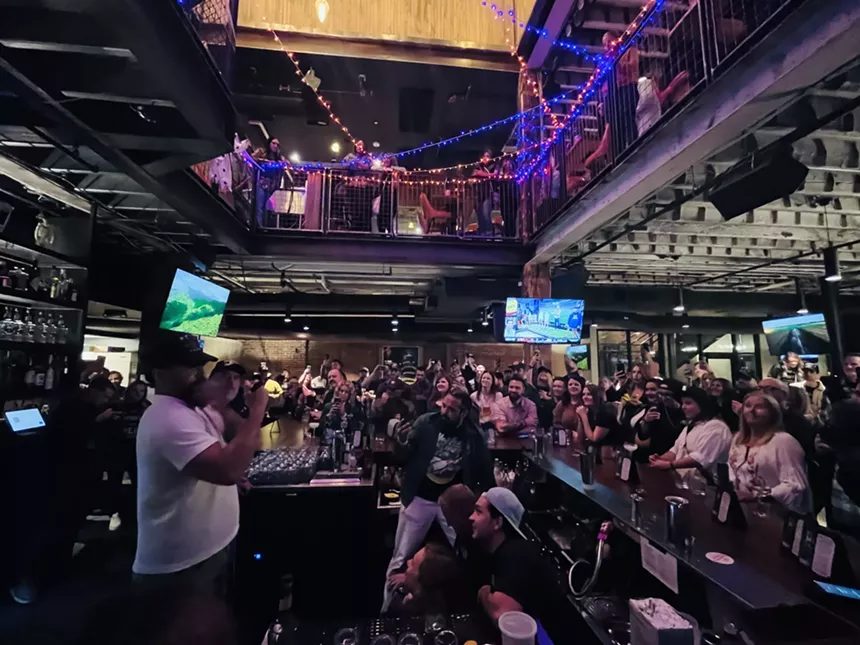 a man in a white t shirt shaking a cocktail behind a crowded bar