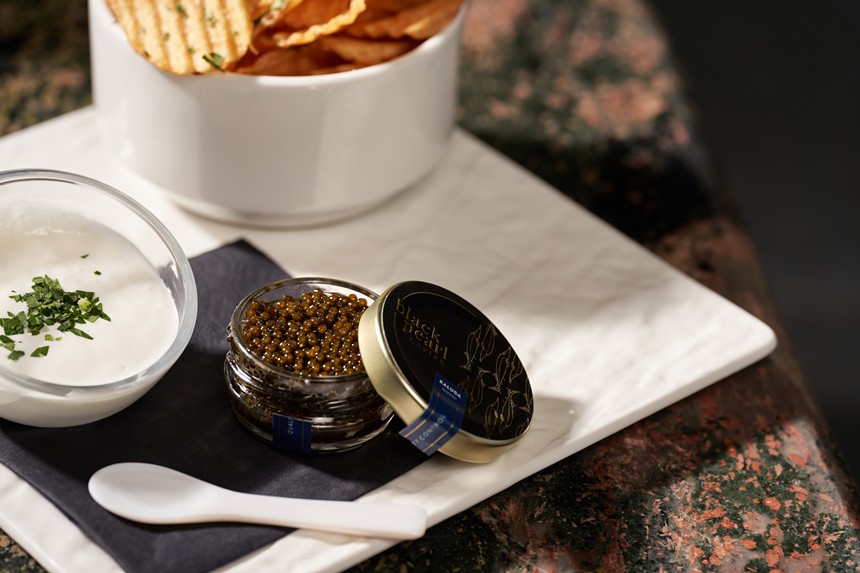 white plate with tin filled with caviar and side of potato chips