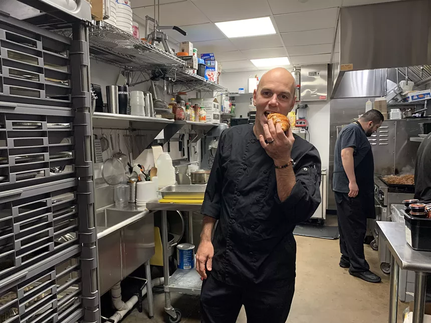a man in a black chef coat eating a croissant