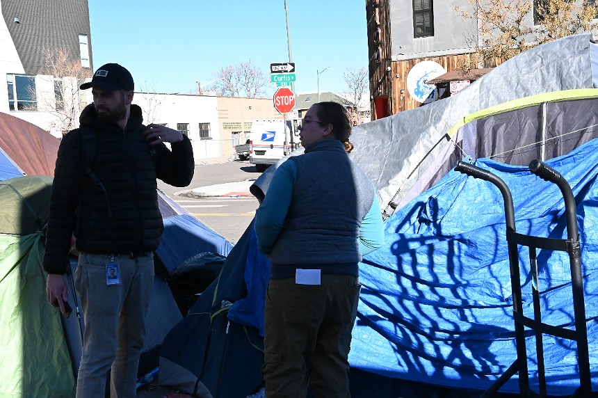 Two city outreach workers wait outside a homeless resident's tent.