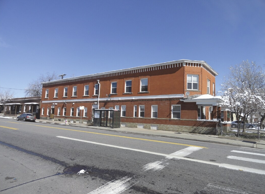 An orange-brick building covered in snow sits beside an empty multi-lane street.