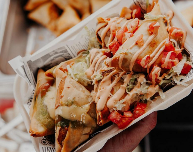 samosas in a to go box with sauce drizzled on top