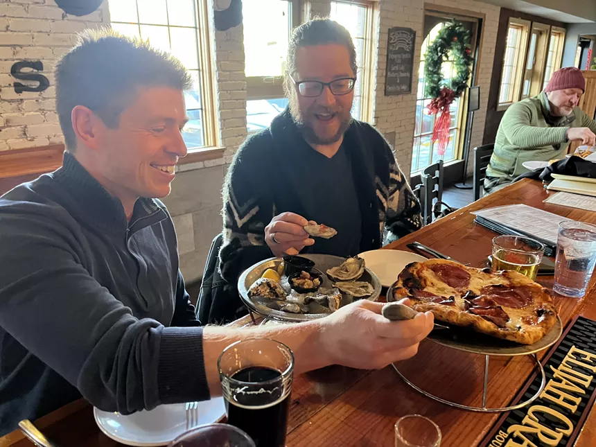 two men eating oysters and pizza