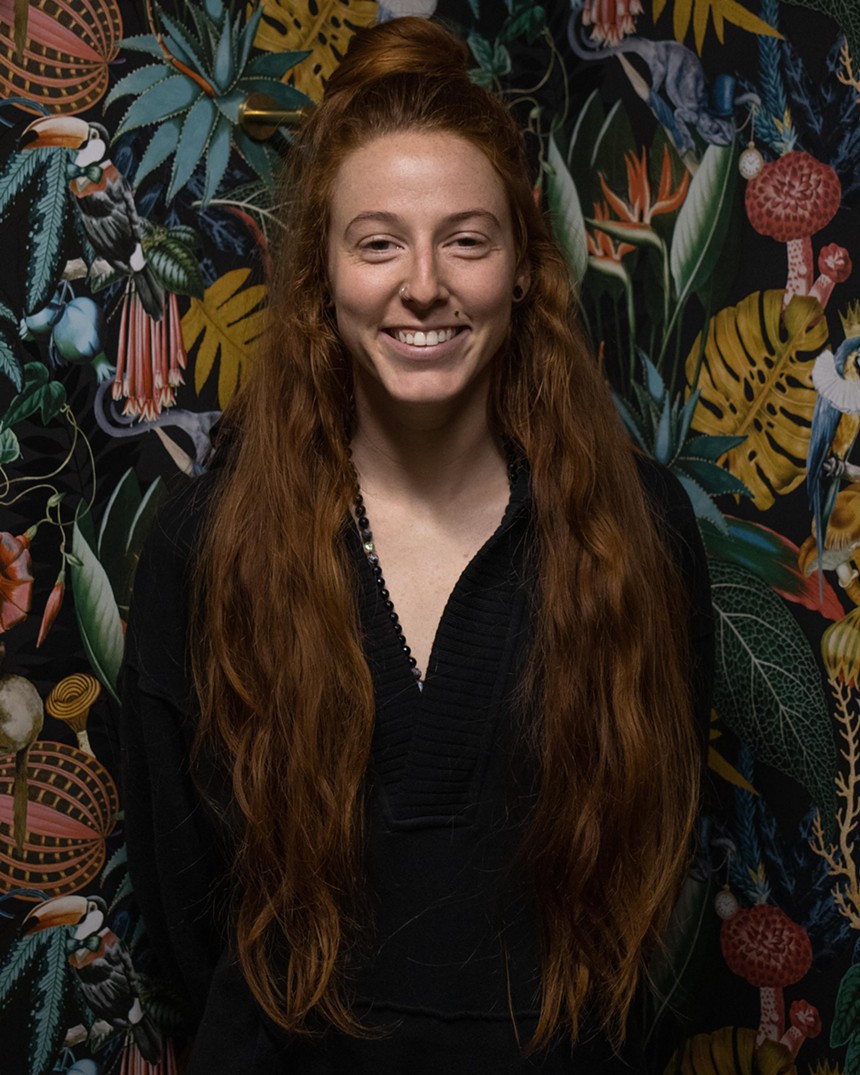 woman with red hair smiles in front of tropical wallpaper